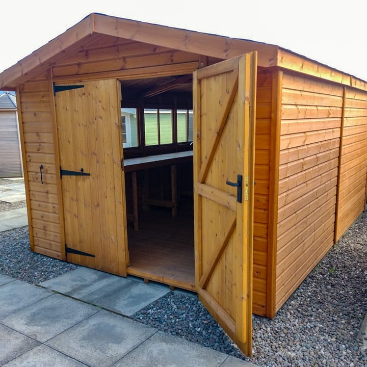 This 10ft x 14ft Heavy Duty Apex is constructed in heavy duty redwood cladding. A roof overhang and opening windows(s) are standard features. Ironmongery is available in a choice of chrome or as pictured here black. Optional felt tiles, double doors and a workbench have all been added.