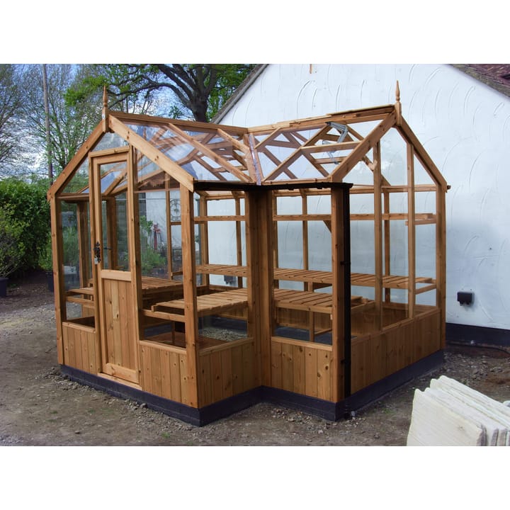 6ft 8in deep x 11ft 5in wide Swallow Cygnet t-shaped greenhouse. The Cygnet incudes front returned staging which sits at the front of the greenhouse and wraps around into the porch area. Optional 'Oiled finish' has been applied to the ThermoWood timber. Optional additional staging and high level shelving to the rear has been added. The Cygnet can be constructed in either dwarf wall format or as pictured here freestanding. There is no extra cost for the dwarf wall option.