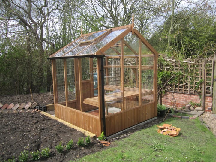 This 6ft x 6ft Kingfisher greenhouse is manufactured from Thermowood. Staging to one side and automatic roof vents are a standard feature.

Optional high level shelving, guttering and additional staging to the rear has been added to this greenhouse
