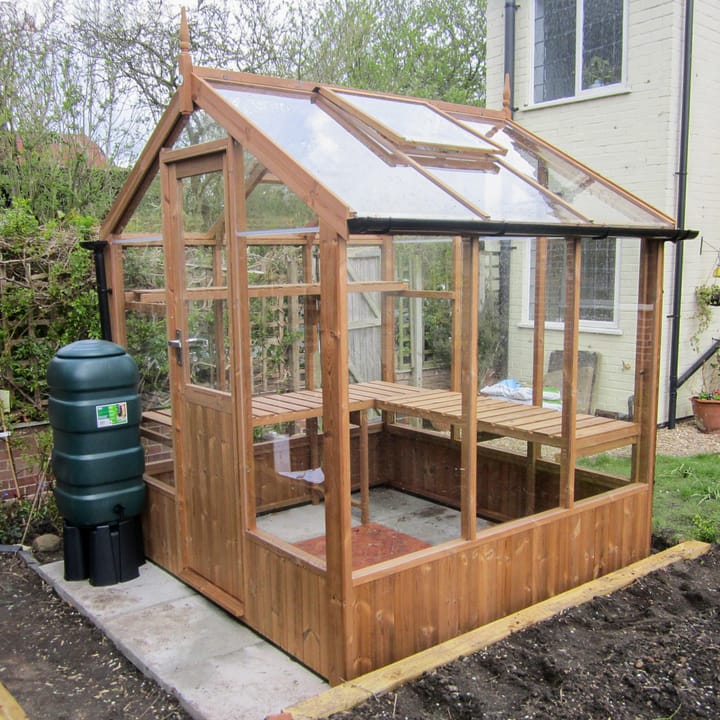 This 6ft x 6ft Kingfisher greenhouse is manufactured from Thermowood. Staging to one side and automatic roof vents are a standard feature.

Optional high level shelving, guttering and additional staging to the rear has been added to this greenhouse