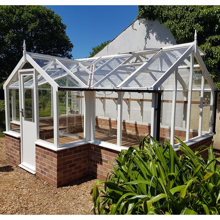 8ft 9in deep x 15ft 9in wide Swallow Mallard t-shaped greenhouse. The Mallard incudes front returned staging which sits at the front of the greenhouse and wraps around into the porch area. Optional 'Lily white painted finish' has been applied to the Thermowood timber.  The Mallard can be constructed either freestanding or as pictured here onto a dwarf wall. There is no extra cost for the dwarf wall option.