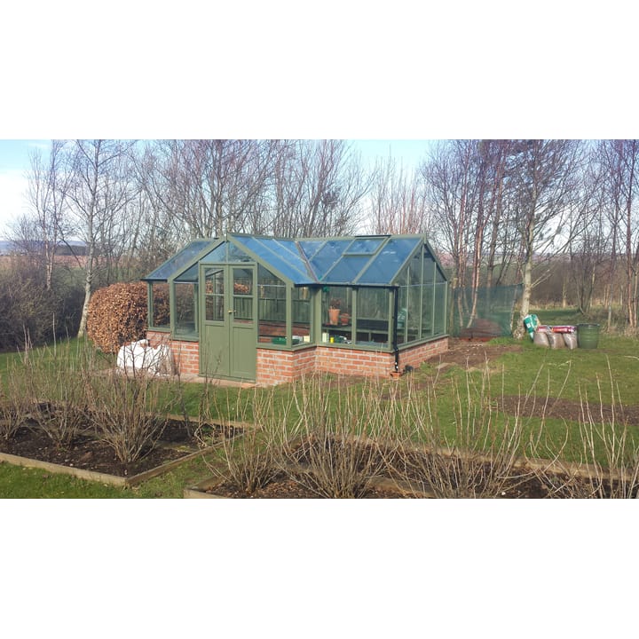 8ft 9in deep x 17ft 10in wide Swallow Swan t-shaped greenhouse. The Swan incudes front returned staging which sits at the front of the greenhouse and wraps around into the porch area. Optional 'Bracken' painted finish has been applied, as has additional staging to the rear. The Swan can be constructed either freestanding or as pictured here in dwarf wall format. There is no extra cost for the dwarf wall option.