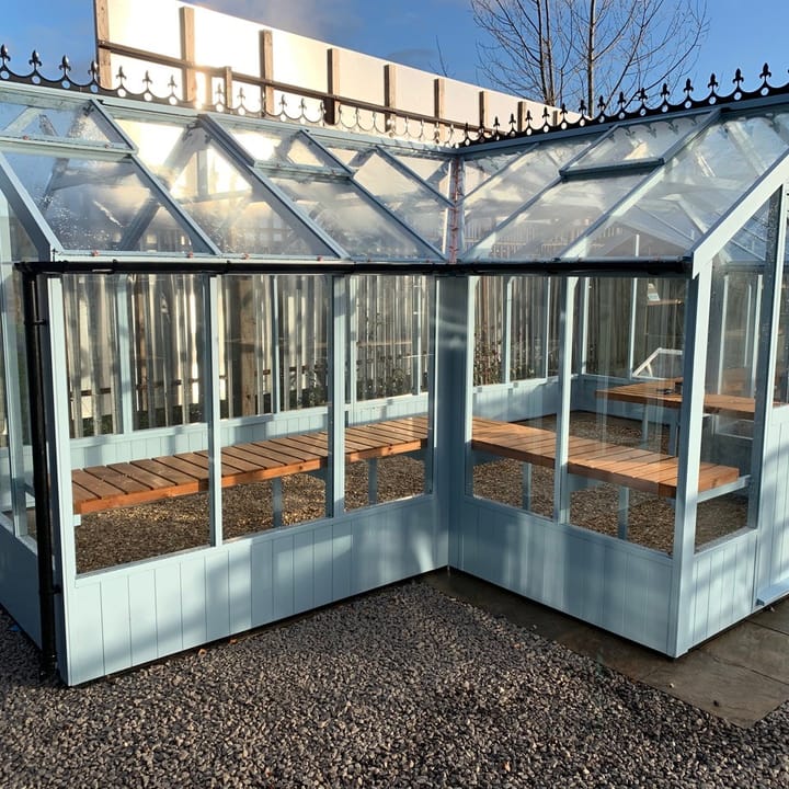 8ft 9in deep x 21ft 1in wide Swallow Swan t-shaped greenhouse. The Swan incudes front returned staging which sits at the front of the greenhouse and wraps around into the porch area. Optional 'Lulworth Blue' painted finish has been applied. The Swan can be constructed in either dwarf wall format or as pictured here freestanding. There is no extra cost for the dwarf wall option.