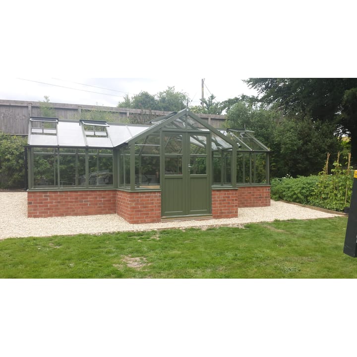 8ft 9in deep x 21ft 1in wide Swallow Swan t-shaped greenhouse. The Swan incudes front returned staging which sits at the front of the greenhouse and wraps around into the porch area. Optional 'Bracken' painted finish has been applied. The Swan can be constructed either freestanding or as pictured here in dwarf wall format. There is no extra cost for the dwarf wall option.
