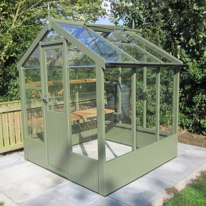 This 6ft x 6ft Kingfisher greenhouse is manufactured from Thermowood. Optional 'Bracken' painted finish has been applied. Staging to one side and automatic roof vents are a standard feature. Optional high level shelving and guttering has been added to this greenhouse.